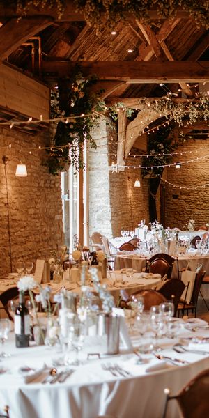 A summer barn wedding breakfast with round tables, white tablecloths and beautiful muted florals. By Kayley Bull Photography.