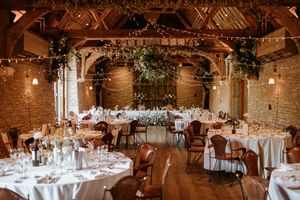A summer barn wedding breakfast with round tables, white tablecloths and beautiful muted florals. By Kayley Bull Photography.