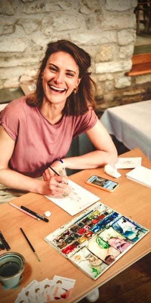 Jo smiling happily whilst painting portraits with watercolours. Photo by Adam Jervis Photography 