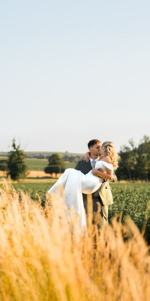 A romantic golden hour portrait of a groom sweeping his bride into his arms in a sunlit countryside meadow, framed by tall golden grass by Alex Gell Photography.