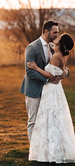 Bride in floral lace wedding dress with groom in grey suit share a kiss before their mariachi band wedding entertainment.