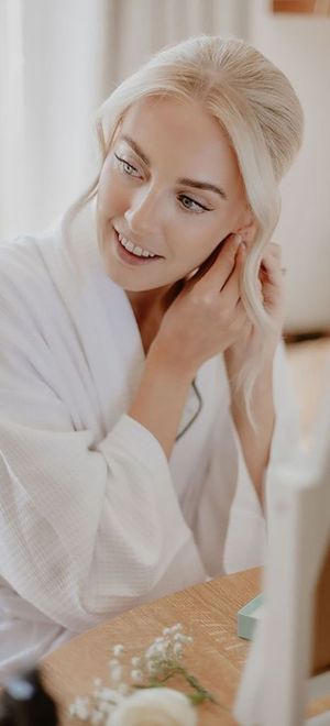 Bride in white waffle robe with blonde hair in an updo with radiant, glowy skin and makeup