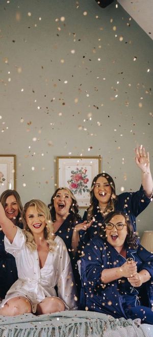 Bridesmaids in satin navy robes and pyjamas popping gold confetti canon as they get ready together