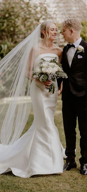 Mermaid wedding dress worn by the bride standing with groom in black tux