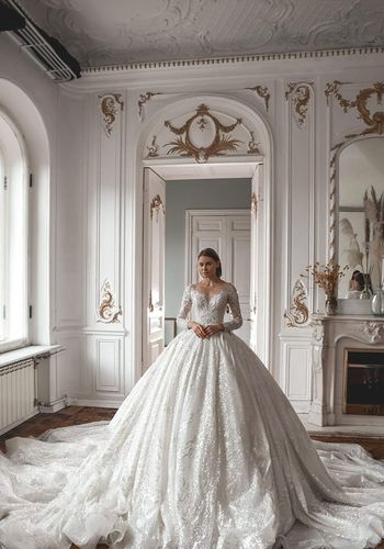 Princess wedding dress with plunging V-neck, hand-embellished with rhinestones, pearls, and crystals. Long sleeves, off-the-shoulder design, and flowing skirt with train.