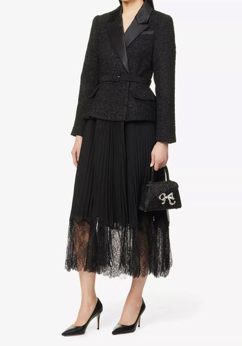 two-piece, jacket style black midi winter wedding guest dress, with padded shoulders, long sleeves, all-over metallic textured weave, contrast pleated skirt, and lace trim at hem. 