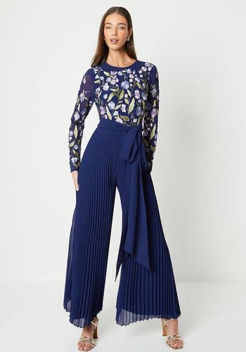 blue wedding guest jumpsuit with floral embroidery, semi-sheer long sleeves, and pleated wide leg trousers.