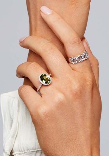 oval peridot sits within a classic four-claw setting surrounded by a diamond halo and shoulders on a white gold band.