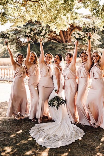 The bride wears a Blue by Enzoani wedding dress with the bridesmaids in blush satin dresses.