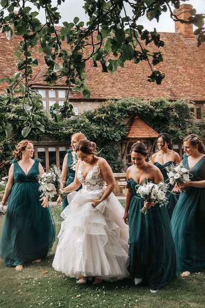 Bride in layered wedding dress walks with bridesmaids in green bridesmaid dresses