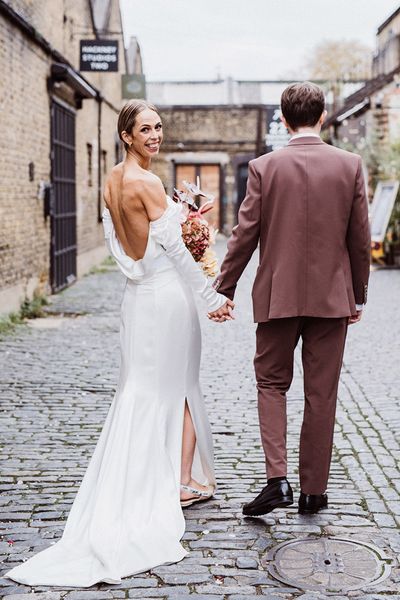 Bride in a cowl neck wedding dress walking with groom in a brown suit.