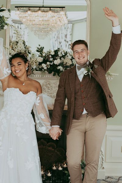 Bride in a floral wedding dress and the groom in a checkered suit in front of faux wedding flower decorations.