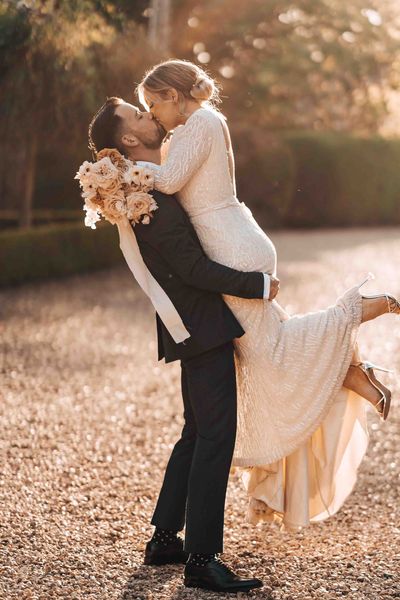 Bride in beaded wedding dress is picked up and kissed by the groom in front of Pennard House wedding venue.