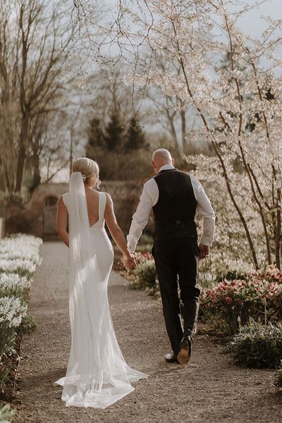 Bride in button back wedding dress from Made With Love walks holding hands with groom around Middleton Lodge for black tie wedding.