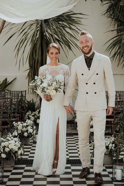 bride in lace Catherine Dean wedding dress with white wedding bouquet stands with husband in beige suit at Gunnesbury Park Orangery wedding altar