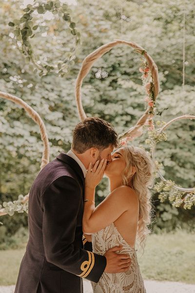 Hula hoop decor for the altar with the bride in a boho lace wedding dress kissing the groom in military uniform. 