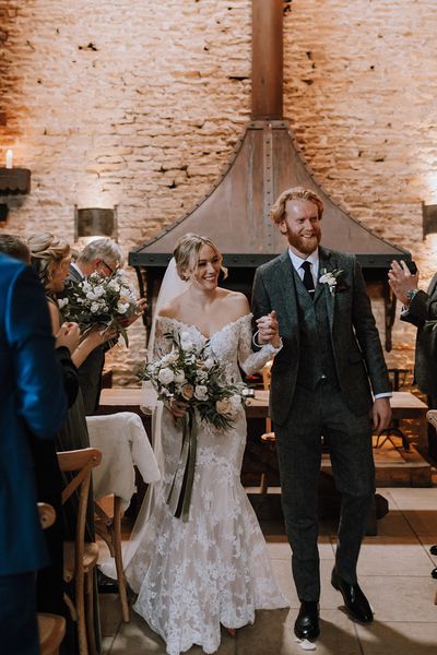 Bride in lace mermaid wedding dress walks back down the aisle with the groom.