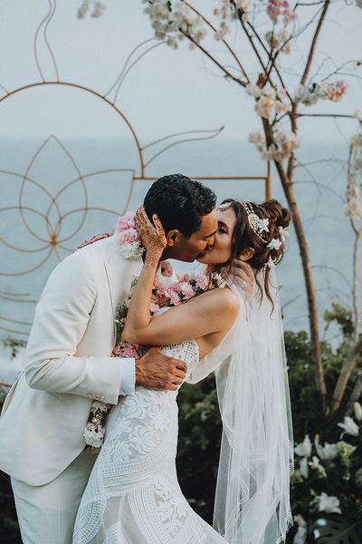 Groom in cream suit kisses bride in boho lace wedding dress and flower hair accessories at Tigre Del Mar wedding in Mexico