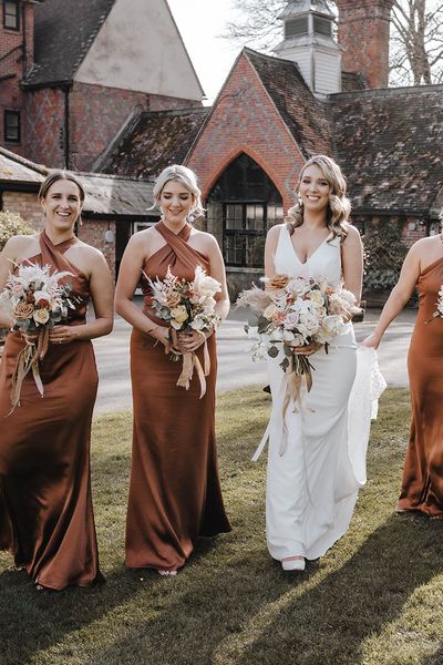 Bride walks with her bridesmaids in stunning satin halter neck copper bridesmaid dresses. 