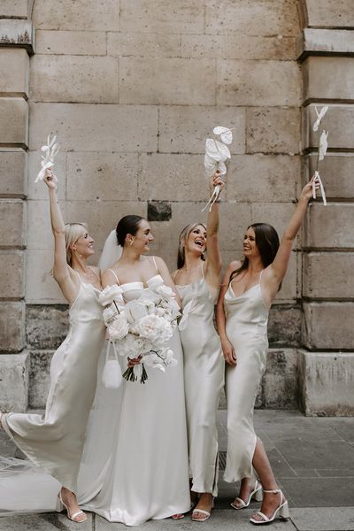 Bride holding white wedding bouquet with bridesmaids in white dresses.