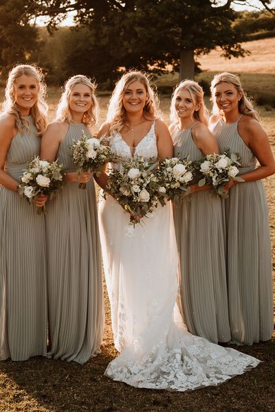 Bridesmaids in sage green pleated bridesmaid dress with the bride for a rustic barn wedding.