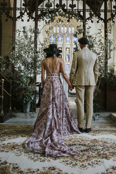 bride and groom wearing pink boho wedding dress and pinstripe groom suit stand at the altar facing away from guests