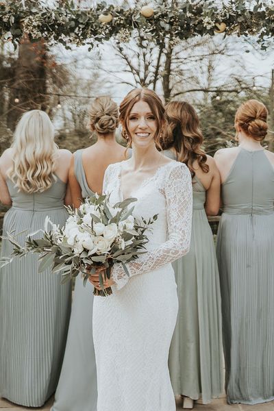 Bride in Maggie Sottero wedding dress holding white wedding flowers with eucalyptus bouquet and bridesmaids in sage green dresses with matching bouquets.