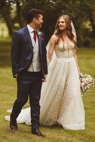 Bride in sparkly Pronovias strapless wedding dress with groom in blue suit and red tie walking together on their wedding day.