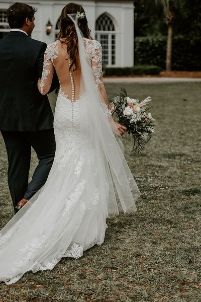 Bride in lace illusion back wedding dress walking holding hands with groom on their wedding day.