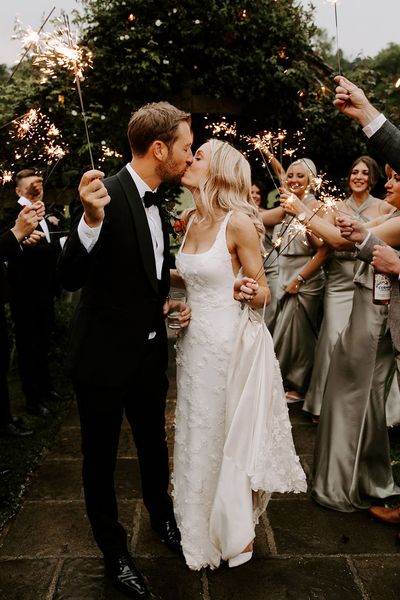 Bride in a 3D applique wedding dress with the groom sharing a kiss for their sparkler send off.