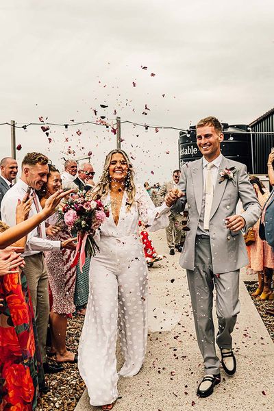 fun east quay Whitstable wedding with bride in a jumpsuit, pink & red colour scheme and mismatched bridesmaid dresses