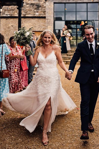 Bride in an Alexandra Grecco Lana wedding dress walking with the groom in a dark blue suit.