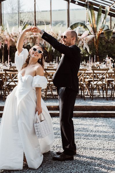 Bride carries a pearl handbag wearing sunglasses in a puff sleeve wedding dress with the groom also in sunglasses.