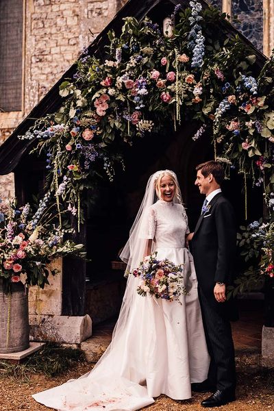 Bride in Jesus Peiro wedding dress and groom in suit stand in front of pink and blue wedding flowers display.