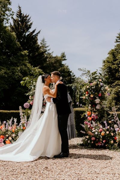 Wootton Hall wedding venue with bride and groom kissing with flower column decor.