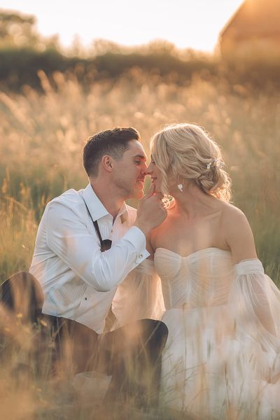 Bride and groom sitting in grass during golden hour at barn wedding