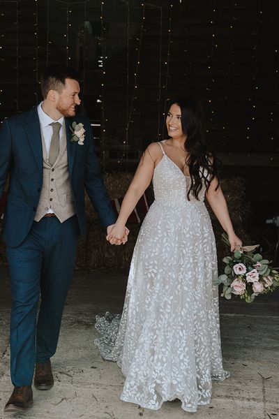 Bride in Madi Lace dress and groom in three piece suit hold hands at The Barns at Farm Lodge. 