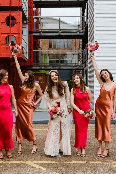 Trinity Buoy Wharf wedding with bride in a lace Rixo dress and bridesmaids in red and orange satin bridesmaid dresses