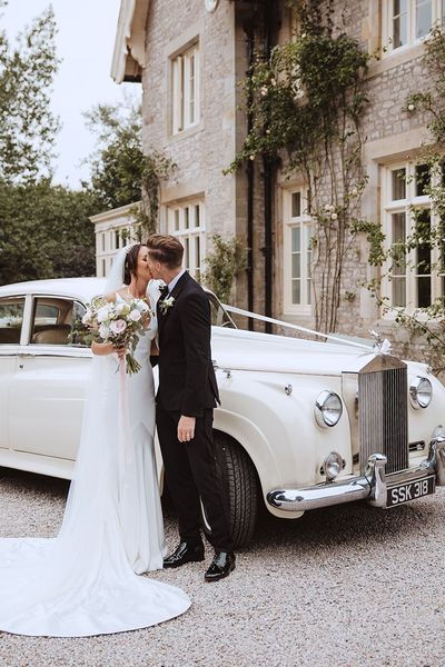 Bride and groom kissing in front of white wedding car at the Casterton Grange Estate venue.