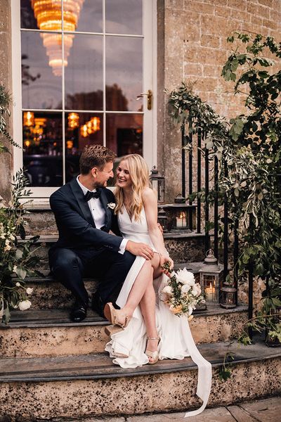 Bride and groom sit smiling on the stairs for their Babington House wedding.