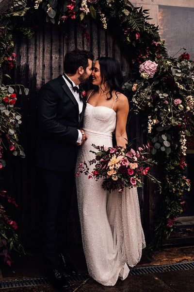 Bride in a beaded sparkle wedding dress with the groom in black tie surrounded by pink flowers.