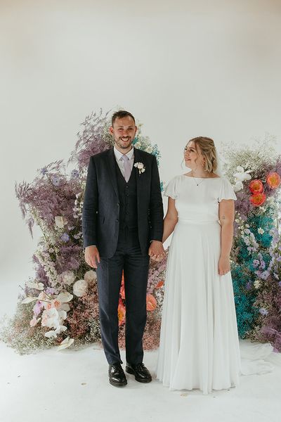 Bride and groom stand holding hands in front of pastel coloured wedding flower columns.