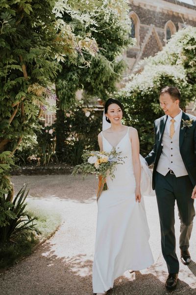 Bride and groom pose together outside their church wedding venue with blue and yellow colour palette as bride wears pearl hair pins and accessories