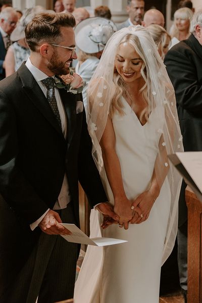 Bride wearing a flower applique veil standing with the groom for their church ceremony.