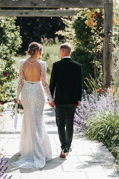 Bride in 3D lace wedding dress with an open back walking with the groom in black tie.