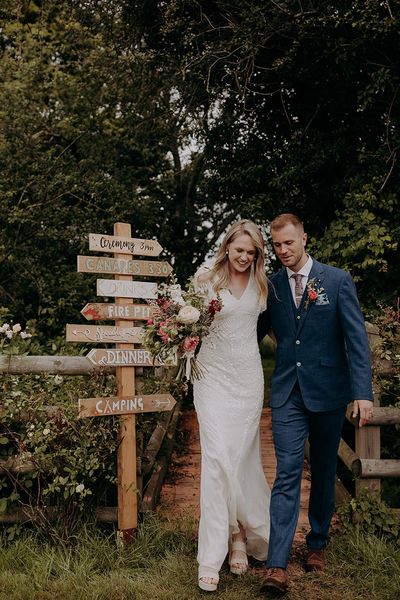 Bride and groom in front of their DIY wedding sign for rustic wedding at barn venue.