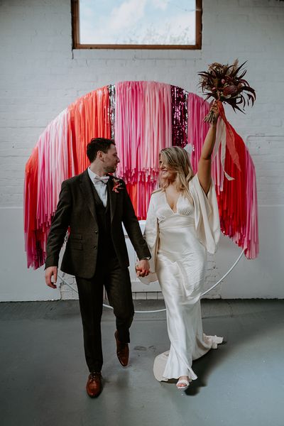 The bride and groom stand in front of pink, red and silver streamer decorations at the altar.