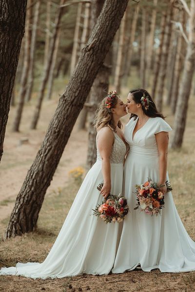 Bride in Freda Bennett wedding dress kissing the other bride for their outdoor wedding.