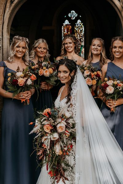 Bride holding cascade wedding bouquet with bridesmaids in navy blue dresses