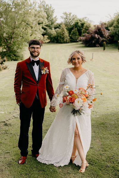 Bride holding an orange and yellow wedding flower bouquet in a boho dress with groom in an orange tux